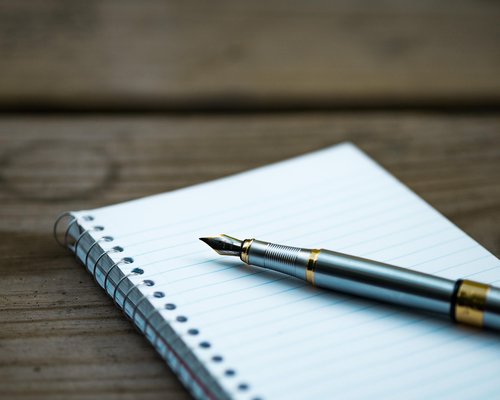 Writing notes in a paper notebook next to a closed laptop